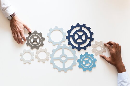 Two hands arranging interlocking gears on a white surface.