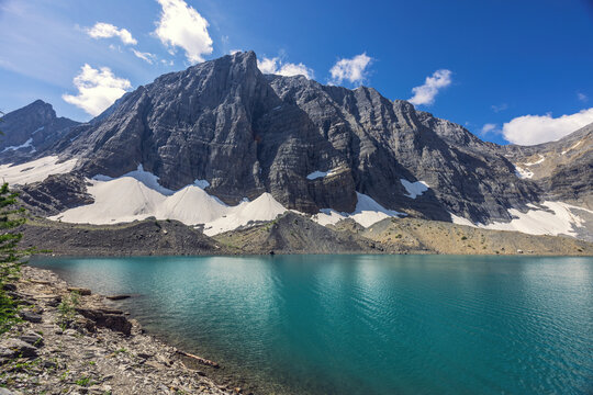 Turquoise alpine lake with rocky mountain cliffs and snowfields under blue sky