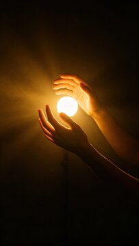Two human hands holding a bright glowing warm light sphere in dark space, conceptual image of hope, energy, magic and life inspiration