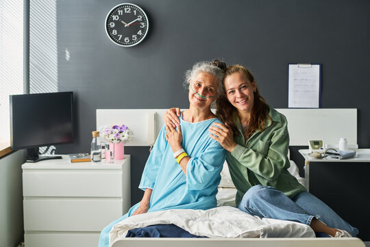 Portrait of senior Caucasian woman patient with nasal cannula and young adult Caucasian daughter smiling in hospital room. Suitable for healthcare marketing