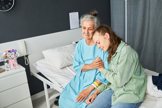 Young adult Caucasian woman visiting senior Caucasian patient in hospital ward, offering emotional support. Ideal for healthcare advertising, elderly caregiving, medical insurance campaigns