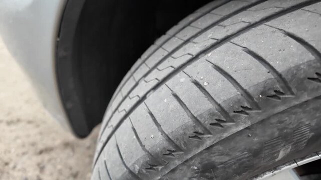Close-up shot of a car tire resting on a dirt and gravel road. The detailed view highlights the rubber tread pattern and the edge of a grey vehicle bumper. Great for auto maintenance concepts.