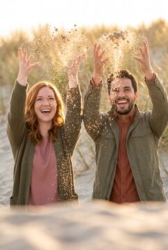 Joyful couple throwing handfuls of sand into the air together at sunset beach