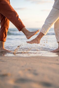 Barefoot couple playing footsie splashing water at sunlit beach shoreline edge