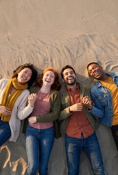 Diverse friends lying on the sand laughing together at golden beach dunes