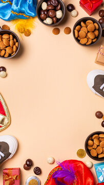 Sinterklaas holiday arrangement features bowls of chocolate and spiced cookies around gifts, shoes on peach surface, top view stories templates with copy space