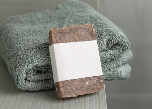 Brown  handmade soap mockup with blank label on sage green towel in bathroom, unbranded packaging