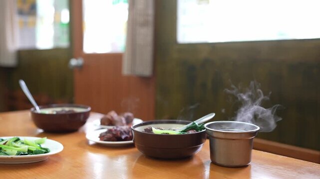 Several prepared dishes and bowls sit on a restaurant table with visible steam rising from hot food.