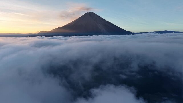 Drone view of Mount Semeru rising above a sea of clouds at sunrise.