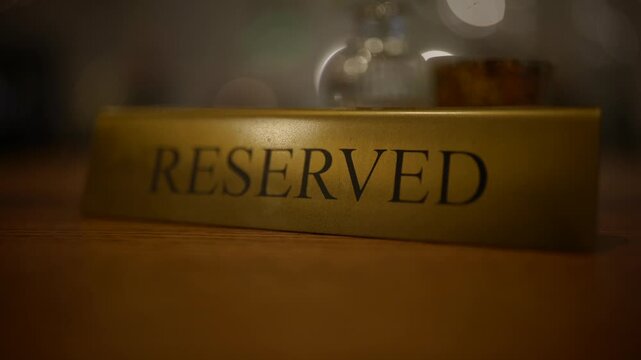 A gold reserved sign sits on a wooden restaurant table in a dimly lit dining room atmosphere