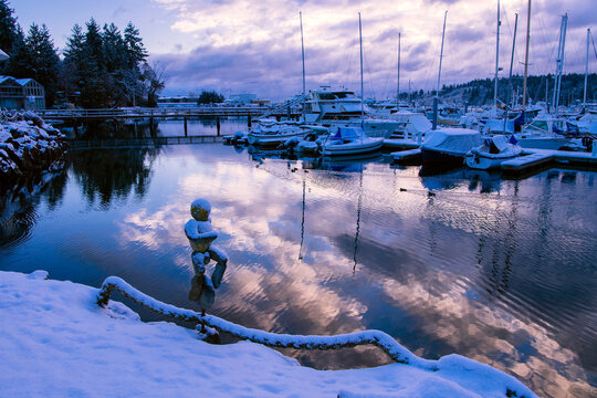 Marina with boats docked in winter snow reflecting clouds in water