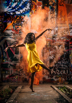 South Asian woman dancing with orange smoke in front of graffiti wall