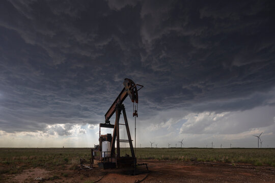 Pump jack under dark storm clouds with wind turbines on Great Plains
