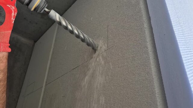 Slow motion close-up low angle video of a heavy duty drill bit penetrating a gas concrete wall for AC installation.