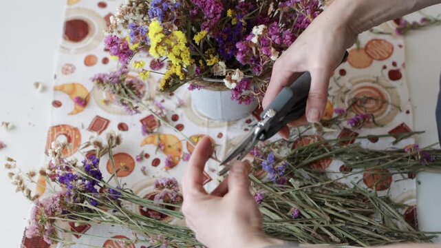 op view of woman hands cutting dried flower stems with secateurs for bouquet composition on table