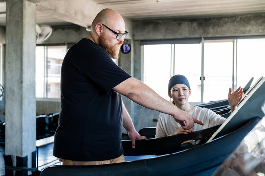 Trainer guiding a gym member on a treadmill, demonstrating controls and form in a bright, industrial-style fitness studio.