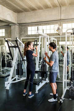 A trainer coaches a woman using a cable machine in a modern gym, emphasizing proper form and strength training.