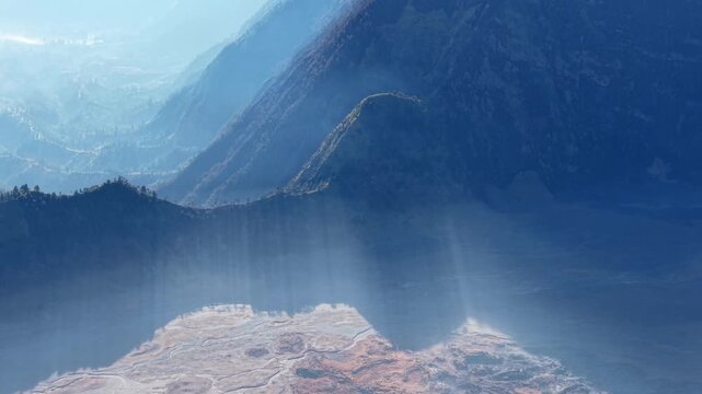Aerial view of misty Bromo ridges and blue volcanic caldera in soft daylight