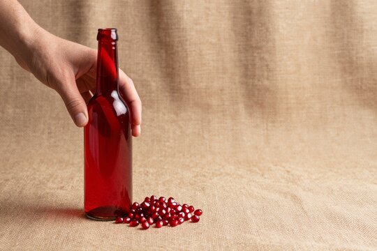 Minimal still life with red glass bottle and fresh pomegranate seeds on coarse burlap fabric