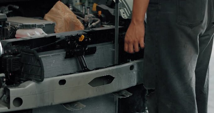 Mechanic cleaning EV radiator and condenser by spraying water and blowing air dry in service garage