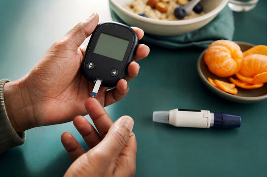 Man measuring blood sugar level with glucose meter at home. Diabetic testing finger with lancet device and test strip near healthy breakfast food.