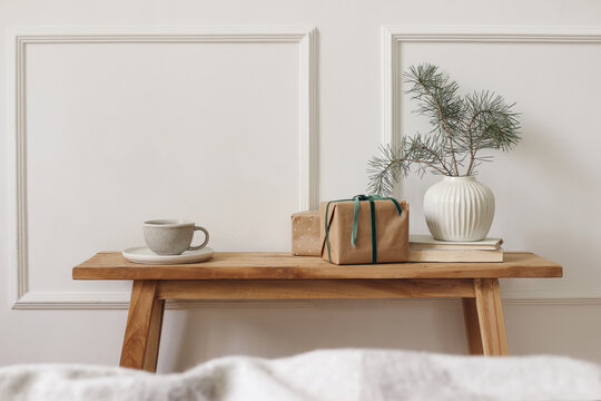 Festive Christmas living room interior still life. Wrapped gifts, Coffee Tea cup on rustic wooden console table. Pine tree branches in ceramic vase. Warm neutral home decor. Winter season holidays