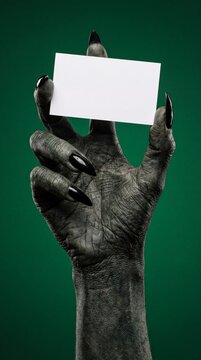 A creepy, gnarled hand with long black claws holds up a blank white card against a dark green background, creating a spooky and mysterious atmosphere.
