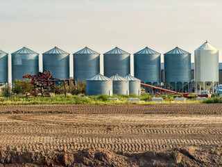 Grain bin storage silos on Saskatchewan prairie farm with tilled field © Uliana