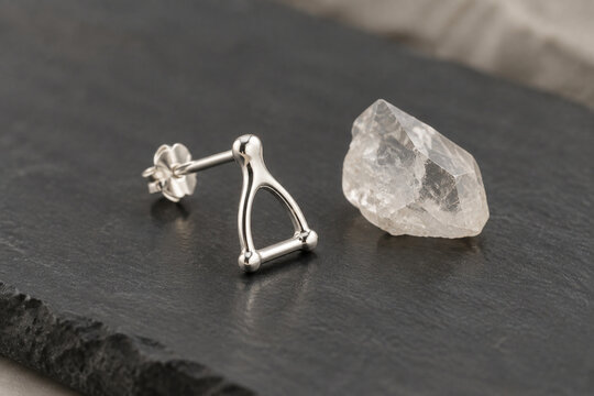 Sterling silver stapes bone earring and quartz crystal on dark slate, jewelry presentation.