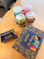 Fototapeta premium Saskachewan, Canada - August 20, 2026: Harry Potter x Tim Hortons limited edition collaboration box and 10-pack timbits with four colorful iced drinks in cardboard carrier on table