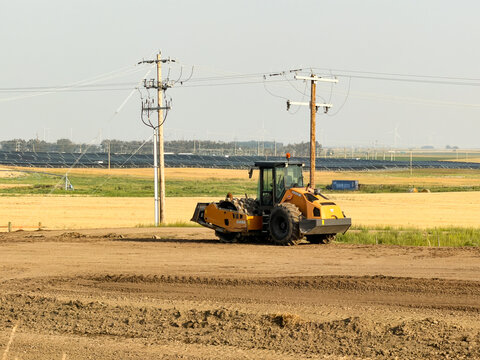 Saskachewan, Canada - August 20, 2026: Case SV213E soil compactor roller grading dirt at renewable energy construction site with solar panels and wind turbines on prairie horizon