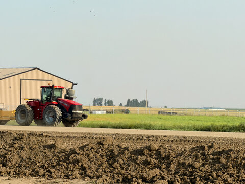 Saskachewan, Canada - August 20, 2026: Red Case IH Steiger articulated tractor driving past farm buildings on rural Saskatchewan prairie farmland with freshly tilled soil foreground