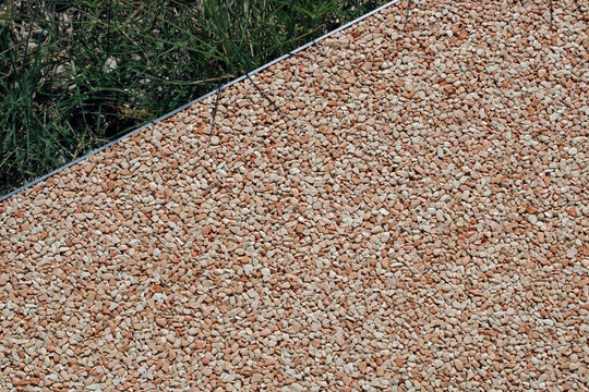 Rev&ecirc;tement de sol ext&eacute;rieur en b&eacute;ton d&eacute;sactiv&eacute; en gravier rose et beige avec bordure m&eacute;tallique discr&egrave;te le long d'une pelouse d'une all&eacute;e