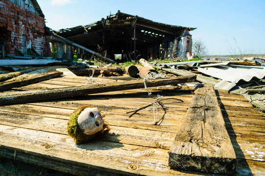 Rural decay background in sunny day. A ruined brick building with a collapsed roof. An old worn toy head lying on weathered wooden planks among debris and dry branches
