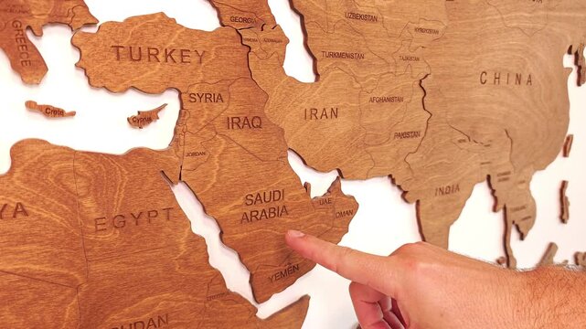 Close up, male hand points to Iran and Saudi Arabia on wooden wall world map referring to the conflict between the two countries