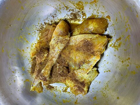 Close up top view of Indonesian Ayam Bumbu Kuning, boiled chicken marinated in yellow turmeric spice in a large metal pan, traditional Asian food preparation