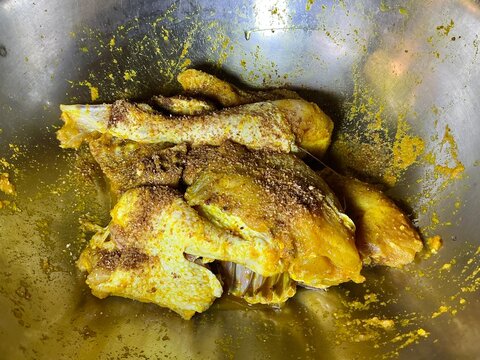 Close up top view of Indonesian Ayam Bumbu Kuning, boiled chicken marinated in yellow turmeric spice in a large metal pan, traditional Asian food preparation
