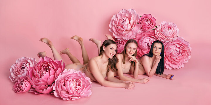 Joyful friends lie together on pink studio floor beside flowing ribbon with warm solidarity. Awareness initiatives, women friendship, healthcare communication concept.