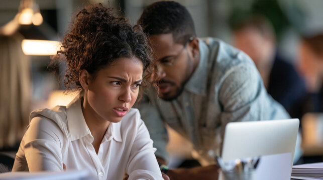 Uncomfortable female employee flinching as a male colleague leans in too close at her desk, tense workplace harassment concept
