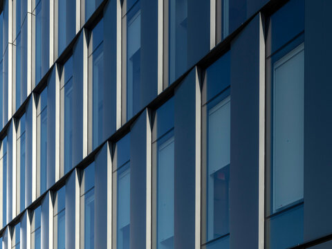Close-up angled view of a curtain wall facade with repeating glass windows and vertical shading fins, receding diagonally across the frame.