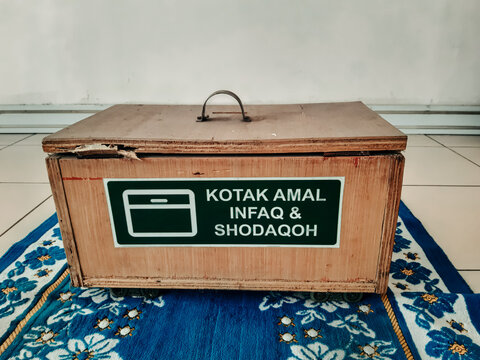 Wooden Islamic donation box on prayer mat with Indonesian text Kotak Amal Infaq Shodaqoh for charity giving.