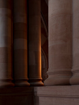 Close-up view of stone columns in low light, with warm reflected light illuminating an ornate archway visible between the columns. 