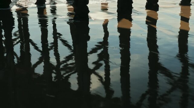 Waves crashing on the shore between the wooden pier columns - slow motion 4K