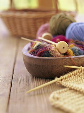 Colorful yarn balls and knitting needles in a wooden bowl on a rustic table with copy space