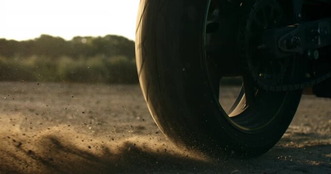 Super slow motion of flying rocks and dust kicked up by the wheel of a sportbike as it accelerates from the start line. Dynamic cinematic motorsport action with speed, power and energy.