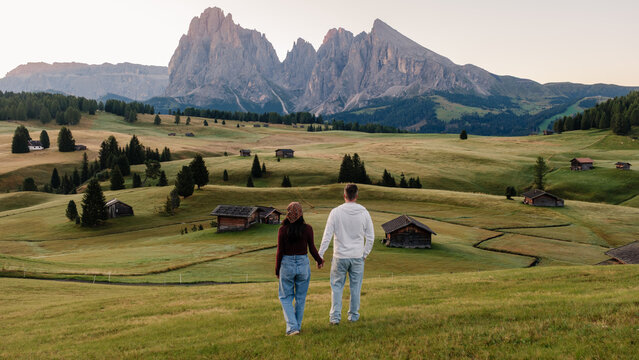 A couple holds hands while strolling through the lush meadows of Seiser Alm, Alpe di Siusi in the breathtaking Dolomites Italy.