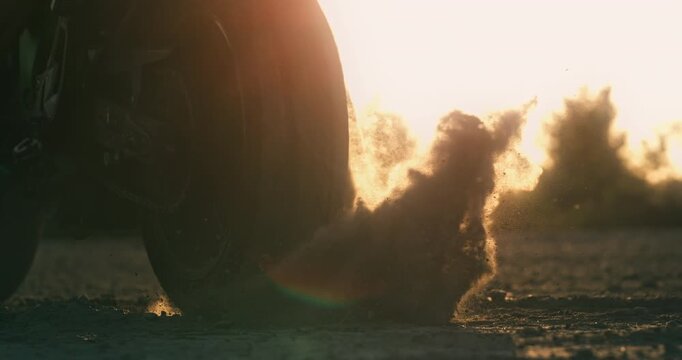 Super slow motion of flying rocks and dust kicked up by the wheel of a sportbike as it accelerates from the start line. Dynamic cinematic motorsport action with speed, power and energy.
