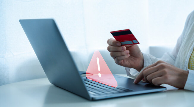 Person holding credit card while using laptop, with warning symbol overlayed, suggests online security concerns