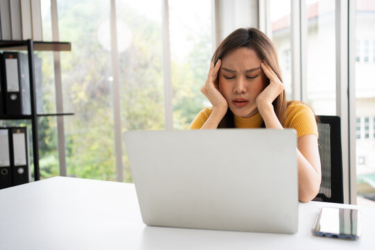 Female professional experiencing stress while working behind a laptop in a bright office, illustrating pressure, frustration, digital workload, and work-life challenges