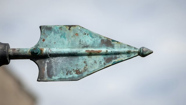 Close-up of Rusty Metal Arrowhead Mounted on a Wood Shaft Against Cloudy Sky